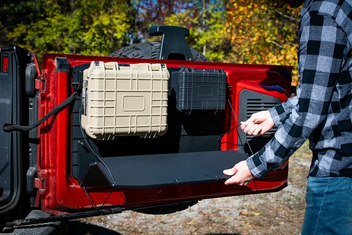 Ford Bronco Tailgate Table A person lowering the Ford Bronco Tailgate Table into position on a red 6th-Gen Bronco, showing the modular storage cases mounted above on the Bronco Tailgate Panel.