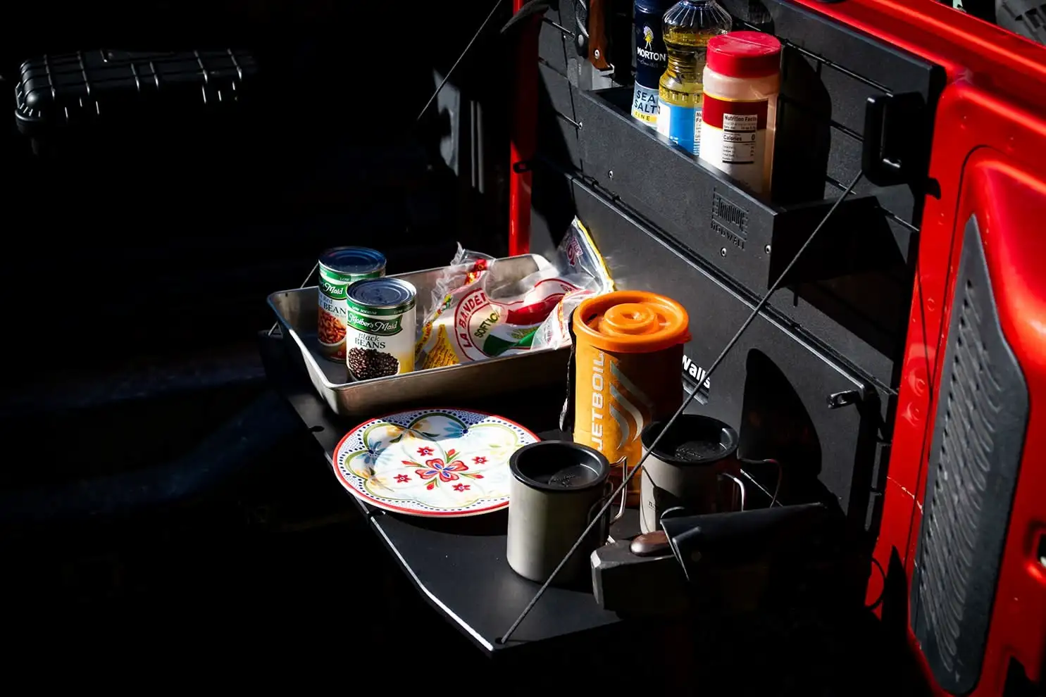 Ford Bronco Tailgate Table High-angle view of the Ford Bronco Tailgate Table holding food prep items and a camp stove, with a large ModWall shelf mounted above for organization.