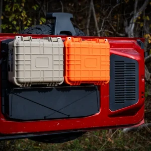 Ford Bronco Tailgate Storage Package An open red Ford Bronco tailgate featuring the modular storage package with two hard-shell gear cases (one orange, one tan) and a folded tailgate table mounted to the black tailgate panel.