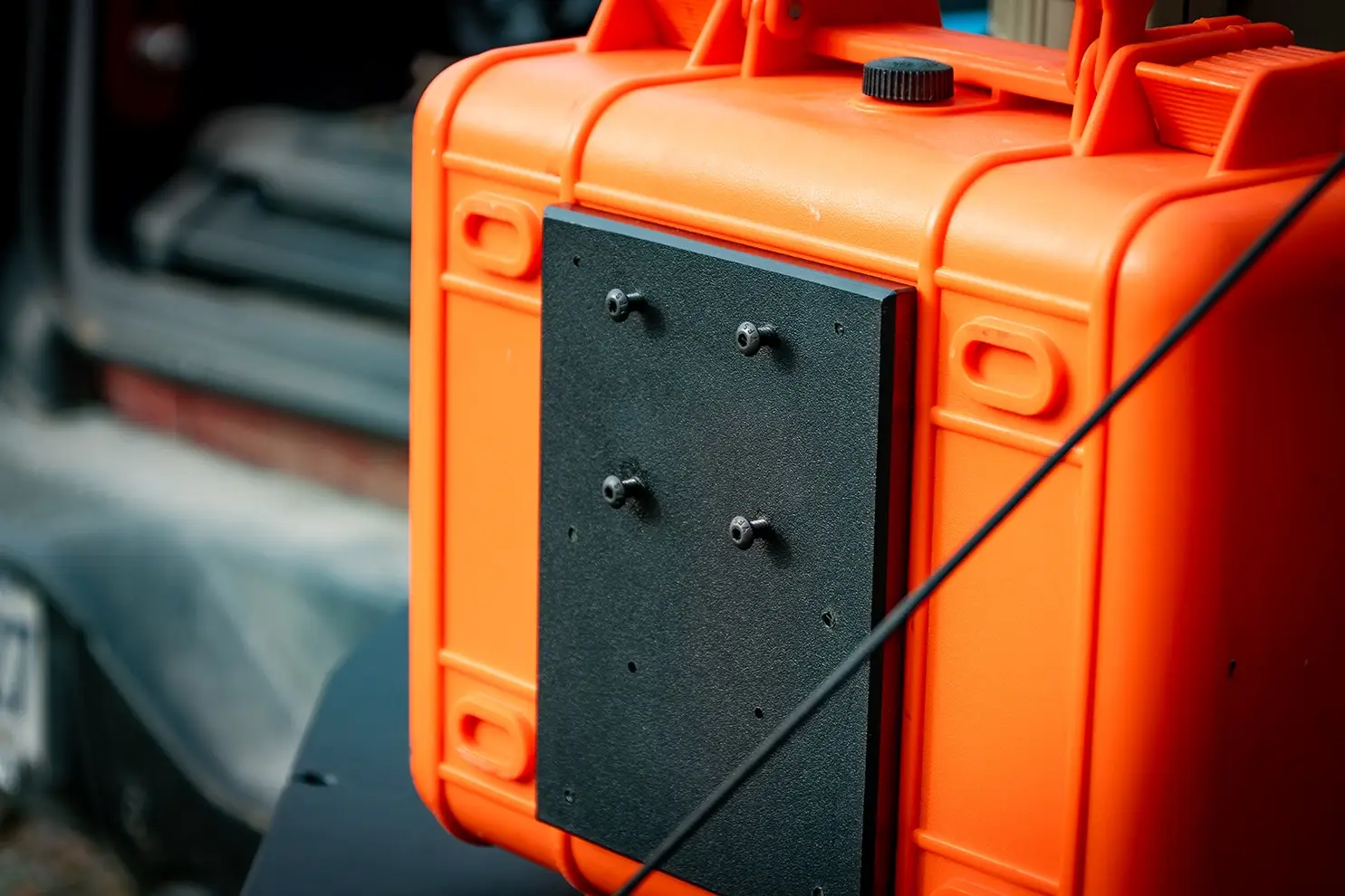 Ford Bronco Tailgate Storage Package Close-up of a black ModWall Case Adapter secured to the back of an orange gear case with four screws, enabling integrated case storage on the Ford Bronco Tailgate Panel.
